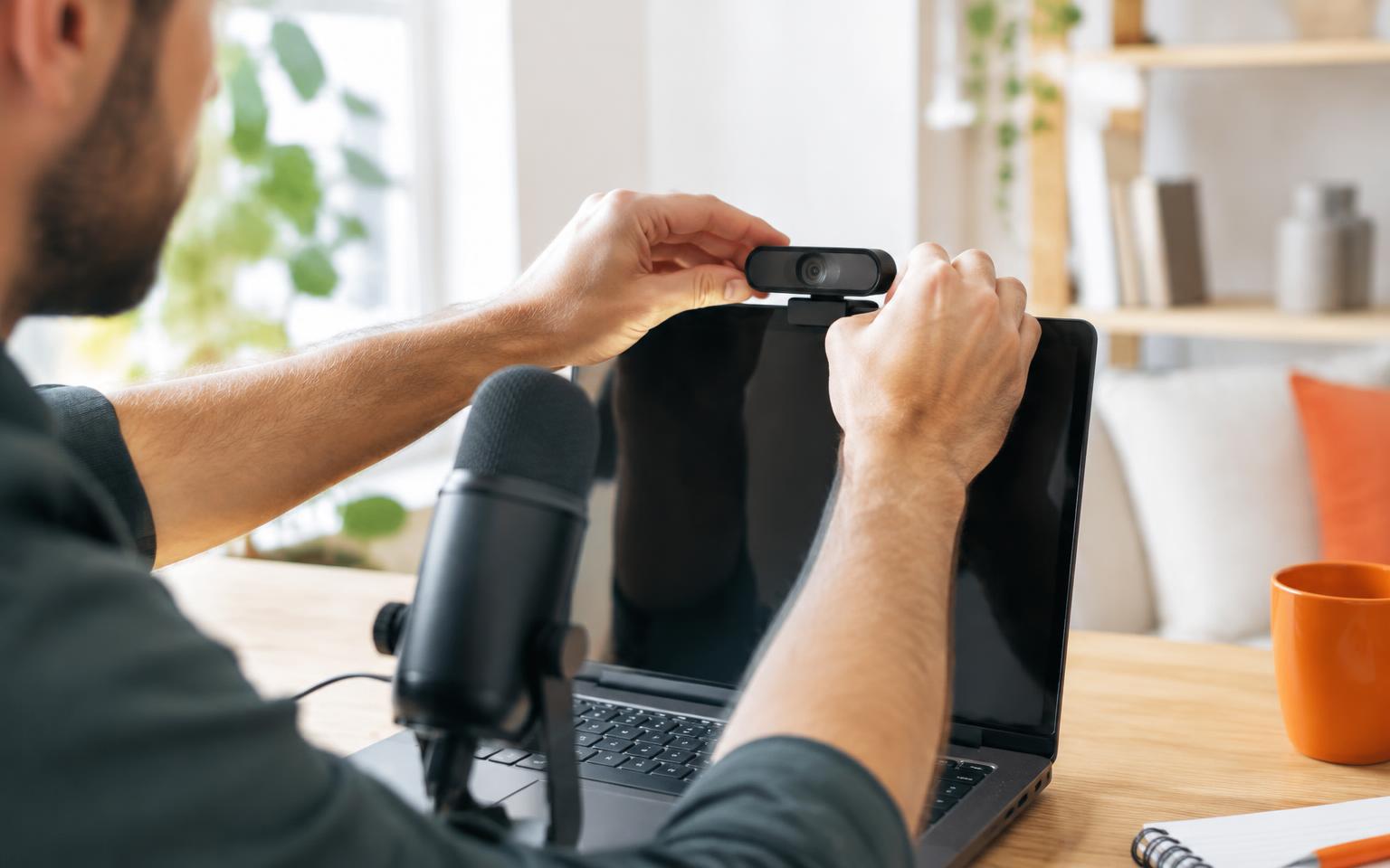 Creator fixing a webcam to the top of his laptop beside a USB microphone while setting up TikTok LIVE Studio